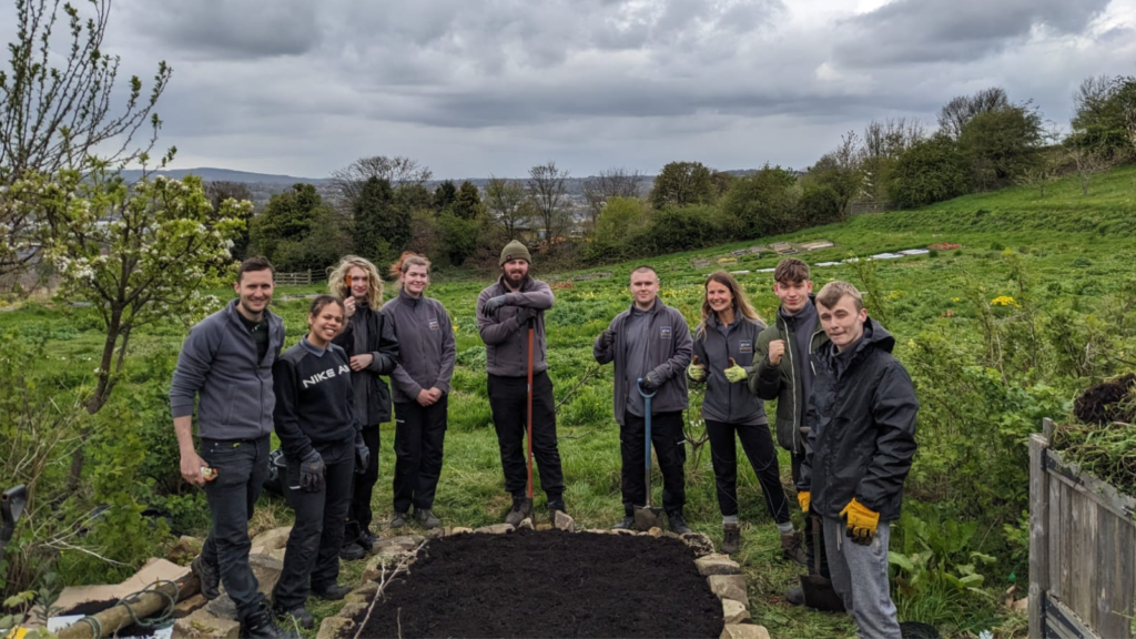 Group of gardeners stood in front of a plant bed with a field in the background.