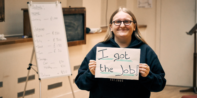 Woman stood smiling and holding a sign that says 'I got the job!'