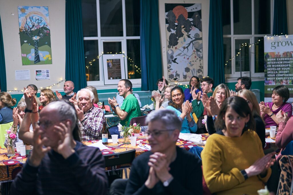 A group of people sat down at an event smiling and clapping their hands. 