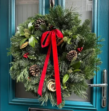 Festive door wreath decorated with green foliage, pine cones, dried fruit and a red ribbon. 