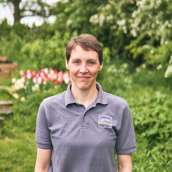 Woman standing outdoors with a garden in the background.