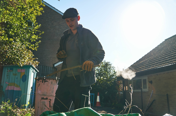 Man wearing grey tshirt and jacket and hat gardening outdoors with the sun in the background_Grow Sheffield